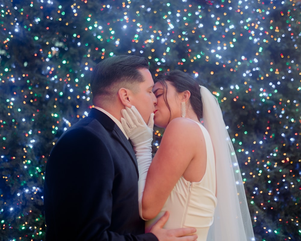 a bride and groom kissing in front of a christmas tree