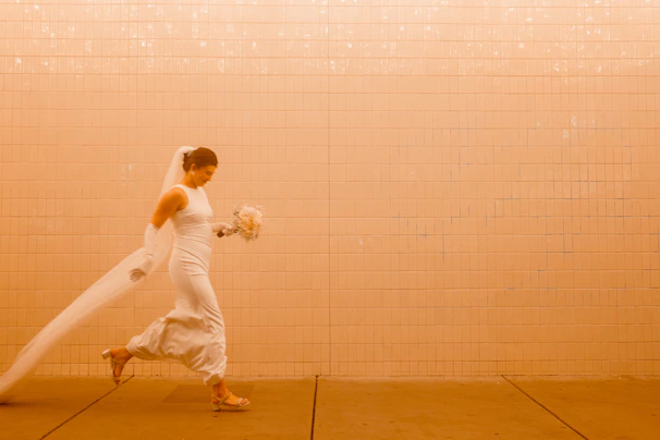 A dramatic black and white portrait of a bride holding a bouquet against a textured wall.