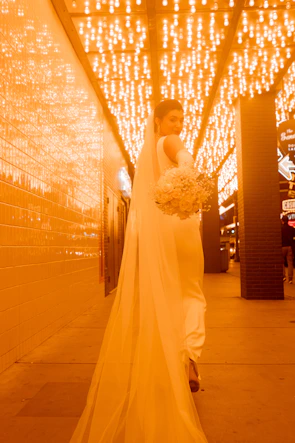 An elegant bride walking down an aisle lined with white and blush floral arrangements.