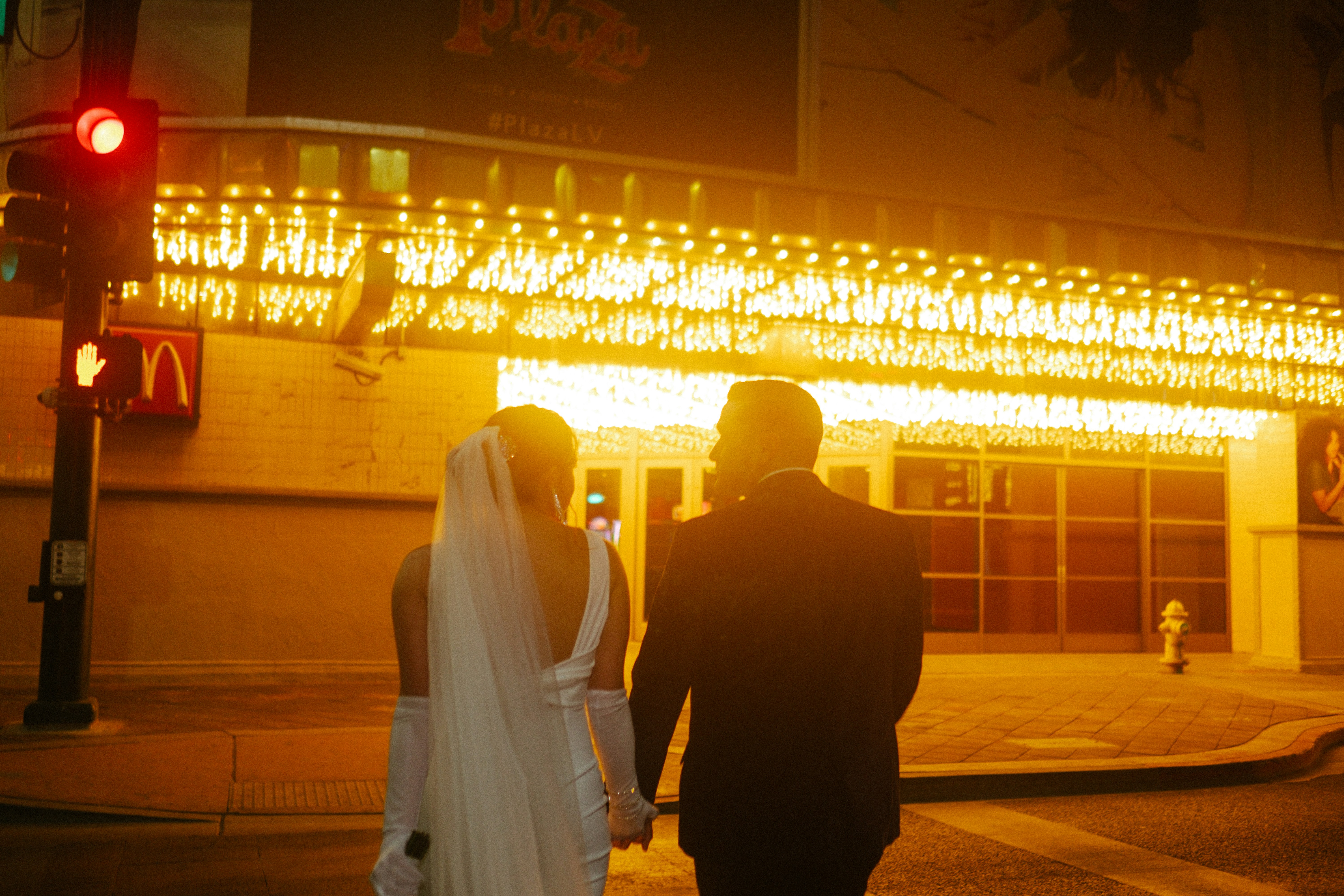 a bride and groom walking down the street at night, 