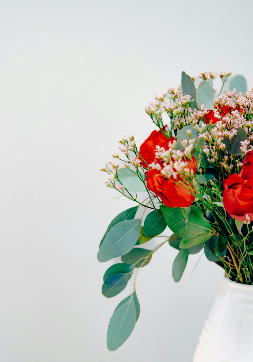 a white vase filled with red roses and greenery