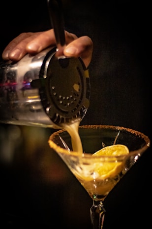 a person pouring a drink into a martini glass