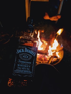 A close-up of a leather-wrapped flask held in a hand against a cozy campfire glow.
