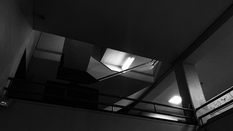 A stark black-and-white photograph of a sleek, minimalist architectural interior featuring sharp lines and expansive empty space.