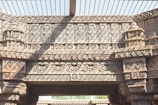 Intricate stone carvings depicting geometric and floral patterns cover the surface of an ancient architectural structure. The design features highly detailed lattice work and symmetrical motifs, characteristic of traditional craftsmanship.