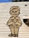 A stylized drawing of a smiling person wearing a uniform with a hat labeled 'BEST' is displayed on a textured, horizontal slatted surface. The figure has exaggerated facial features and is in a greeting posture with hands together.