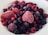 A close-up view of a variety of frozen berries, including strawberries, raspberries, blueberries, and blackberries, covered with a light layer of frost, placed on a white plate.