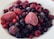 A close-up view of a variety of frozen berries, including strawberries, raspberries, blueberries, and blackberries, covered with a light layer of frost, placed on a white plate.