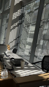 A professional cleaner in uniform sanitizing an office desk with natural light streaming through windows.