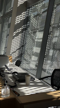 Modern office environment with sunlight streaming through large windows, highlighting tech devices and notes.
