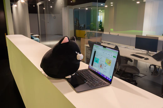 A friendly tech mascot chameleon named Kux interacting with a small business owner in a modern office.