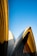 Architectural design with curved, overlapping structures set against a clear, blue sky. The building features a combination of smooth and textured surfaces, with distinct shadows cast by the sun.