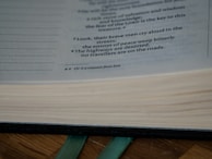 The close-up view of an open book reveals printed text with clear line spacing. The focus is on a portion of a page with highlighted text that reads, 'Look, their brave men cry aloud in the streets; the envoys of peace weep bitterly. The highways are deserted, no travelers are on the roads.' A ribbon bookmark is visible protruding from the bottom of the pages.