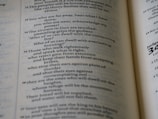 A close-up view of an open book displaying text in English. The text is organized in paragraphs and includes numbered verses, typical of a religious scripture. The paper is slightly off-white, and the typography is clear.