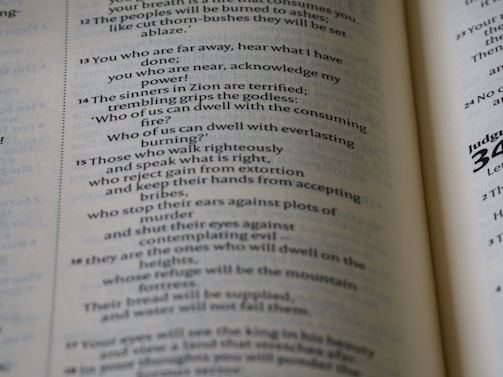 A close-up view of an open book displaying text in English. The text is organized in paragraphs and includes numbered verses, typical of a religious scripture. The paper is slightly off-white, and the typography is clear.