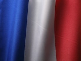 A fabric displaying three vertical stripes of blue, white, and red, representing the French flag. The texture of the material is visible, showing the weave pattern and slight shadows.