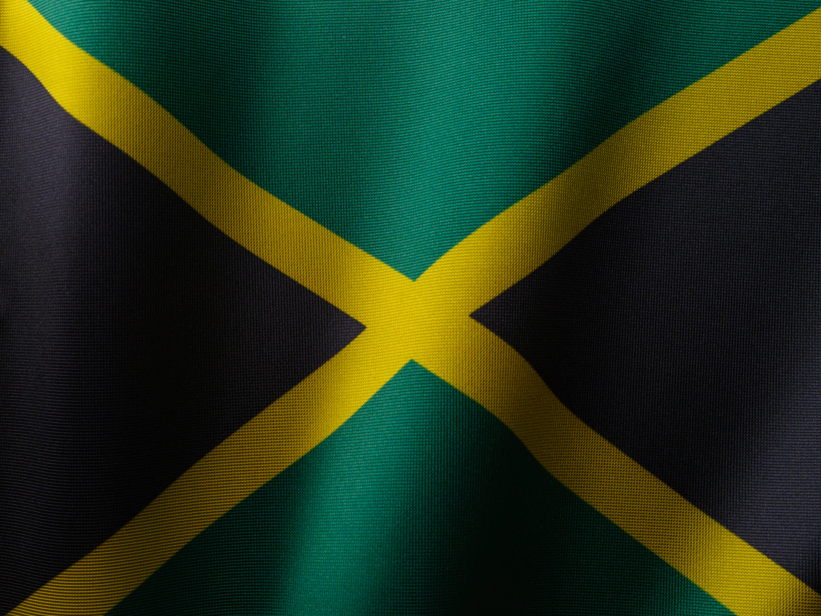 The Jamaican flag, black gold and green, waving against a plain backdrop