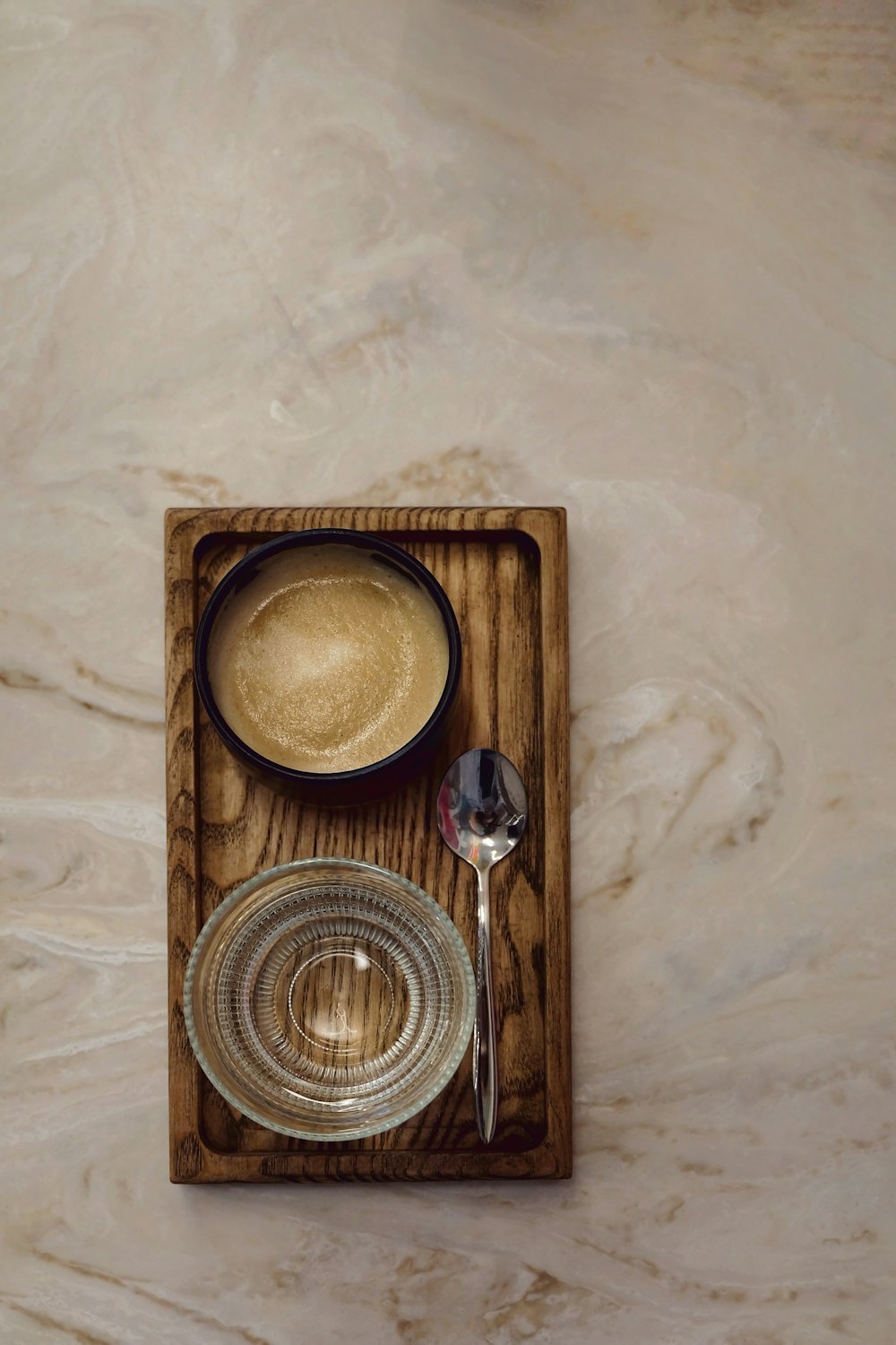 a wooden tray with a glass bowl and a spoon