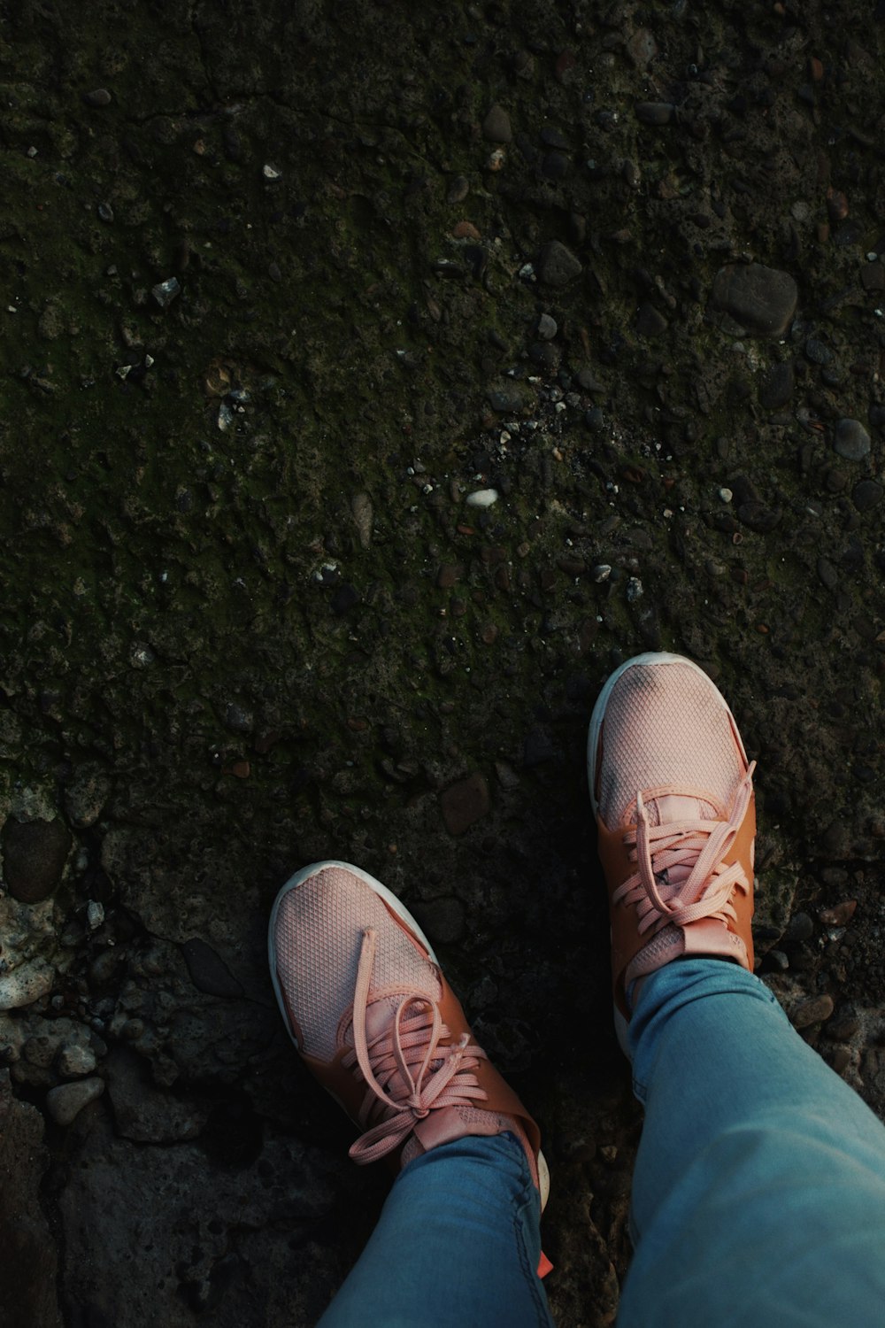 a person wearing pink tennis shoes standing on a rocky ground