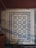 Intricate floor tiles with a decorative pattern, featuring symmetrical design elements in blue and white. The tiles are framed by a diamond border, creating a visually striking appearance. The floor appears aged and shows signs of wear.