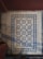Intricate floor tiles with a decorative pattern, featuring symmetrical design elements in blue and white. The tiles are framed by a diamond border, creating a visually striking appearance. The floor appears aged and shows signs of wear.