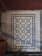Intricate floor tiles with a decorative pattern, featuring symmetrical design elements in blue and white. The tiles are framed by a diamond border, creating a visually striking appearance. The floor appears aged and shows signs of wear.