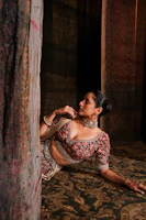 A close-up of a woman wearing a richly embroidered Zard kaftan in warm beige tones, softly lit against a vintage backdrop.
