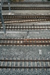 An aerial view of multiple parallel railway tracks laid on a bed of gravel. The tracks are evenly spaced and supported by wooden sleepers. A metal pole is visible to the left side of the image, possibly part of the railway infrastructure.