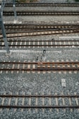 An aerial view of multiple parallel railway tracks laid on a bed of gravel. The tracks are evenly spaced and supported by wooden sleepers. A metal pole is visible to the left side of the image, possibly part of the railway infrastructure.