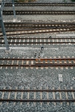 An aerial view of multiple parallel railway tracks laid on a bed of gravel. The tracks are evenly spaced and supported by wooden sleepers. A metal pole is visible to the left side of the image, possibly part of the railway infrastructure.