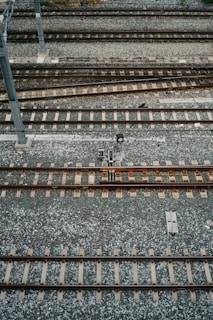 An aerial view of multiple parallel railway tracks laid on a bed of gravel. The tracks are evenly spaced and supported by wooden sleepers. A metal pole is visible to the left side of the image, possibly part of the railway infrastructure.