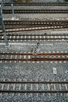 An aerial view of multiple parallel railway tracks laid on a bed of gravel. The tracks are evenly spaced and supported by wooden sleepers. A metal pole is visible to the left side of the image, possibly part of the railway infrastructure.