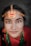 A person wearing traditional jewelry with a prominent chain headpiece featuring crescent and star designs. The attire includes vibrant colors and jewelry, such as a nose ring and necklace. The background is softly blurred, drawing focus to the individual's detailed facial features and adornments.