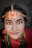 A person wearing traditional jewelry with a prominent chain headpiece featuring crescent and star designs. The attire includes vibrant colors and jewelry, such as a nose ring and necklace. The background is softly blurred, drawing focus to the individual's detailed facial features and adornments.