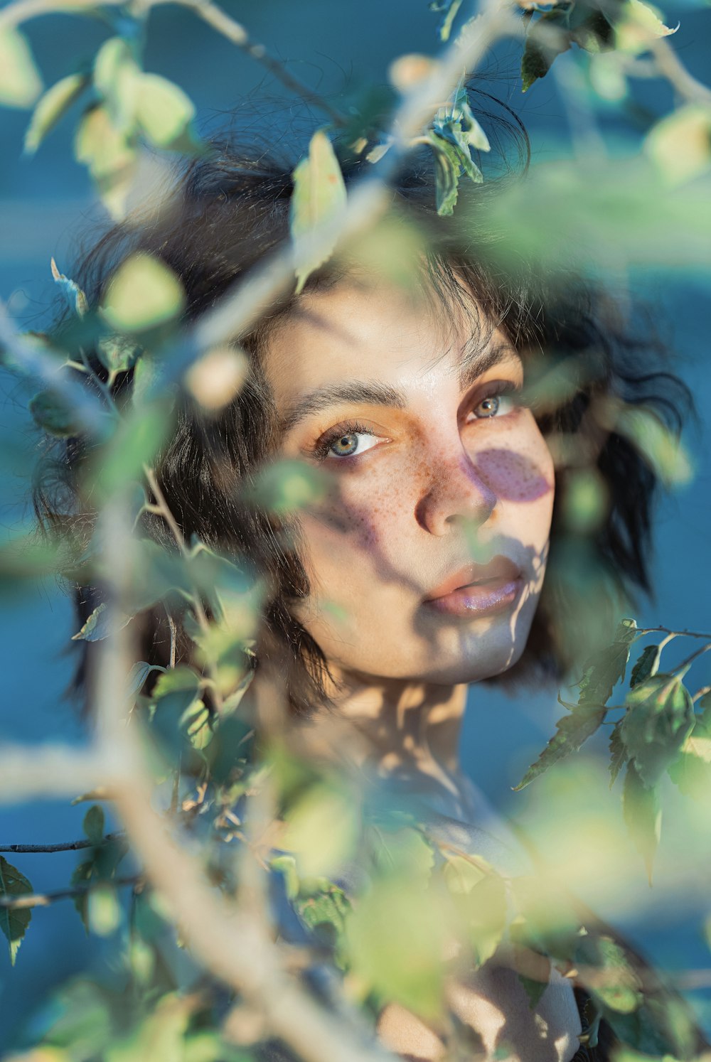 a woman with freckles on her face looking through a tree