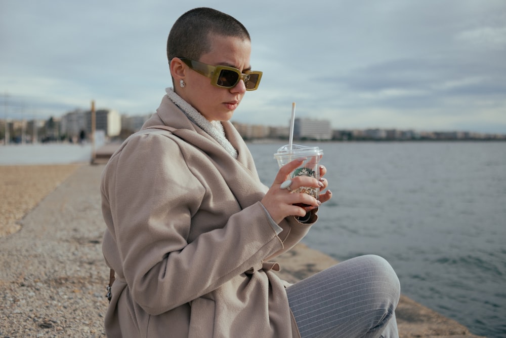 a woman sitting on a beach holding a drink