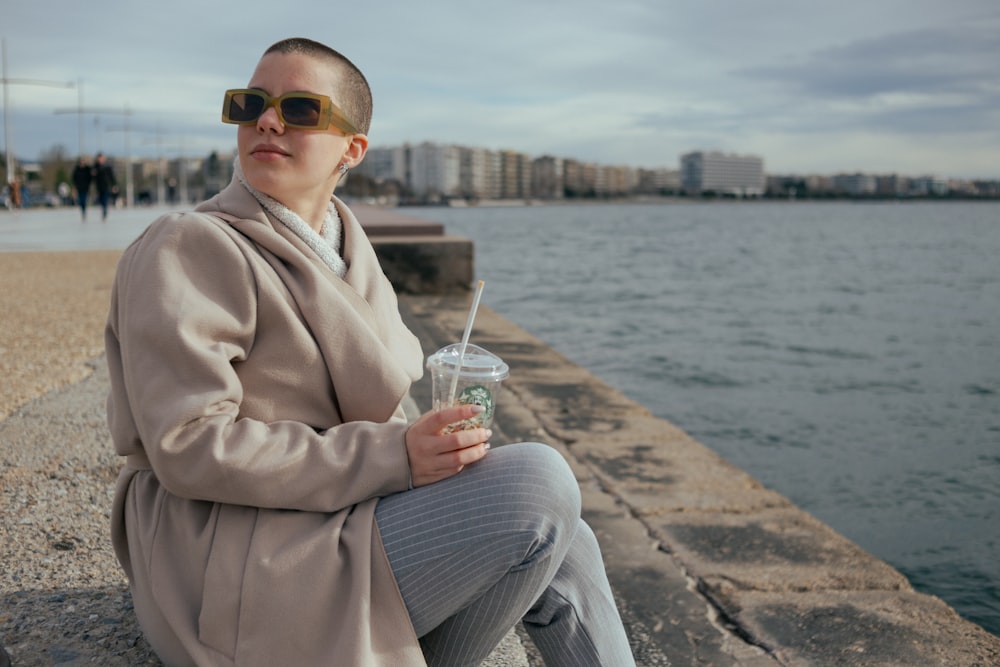 a woman sitting on a ledge next to a body of water