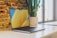 A close-up of a sleek laptop on a wooden desk with a plant in the background.
