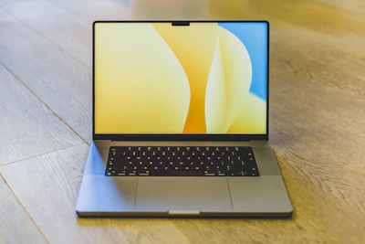 A sleek modern laptop on a clean desk with a yellow mustard accent wall.