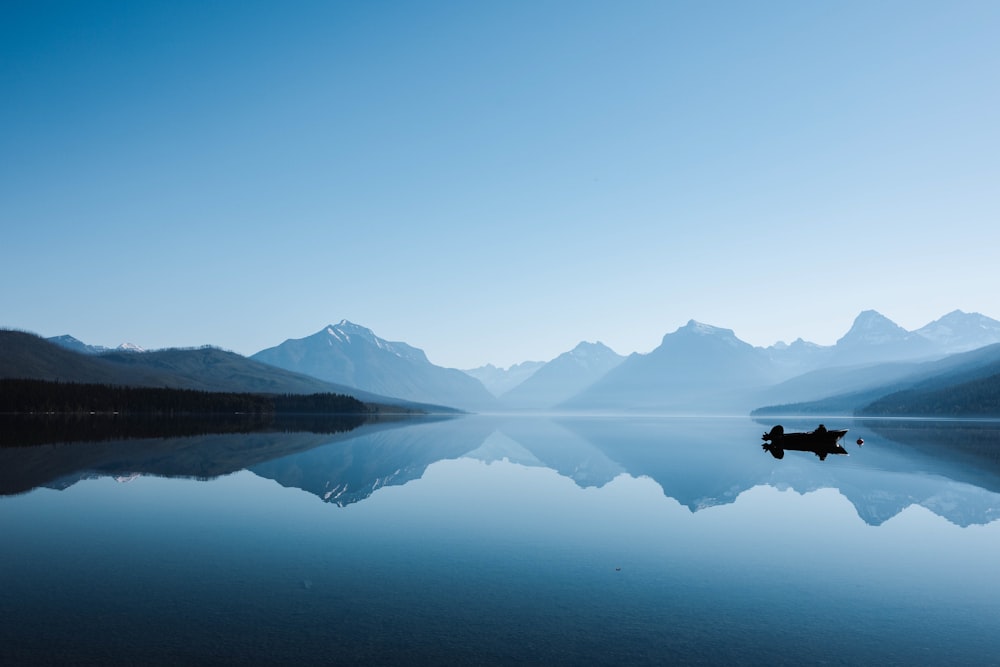 a lone boat floating on top of a lake surrounded by mountains