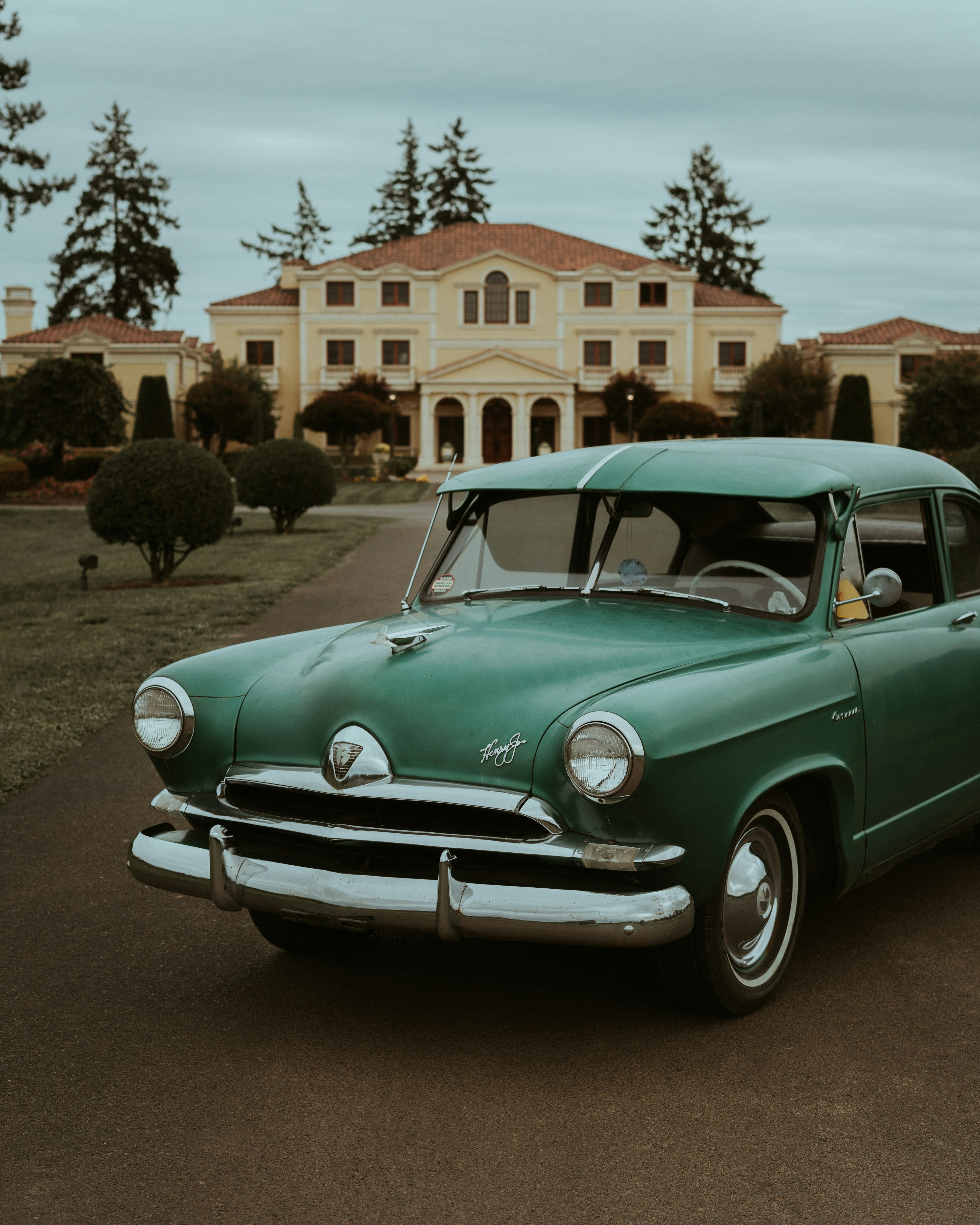 an old green car parked in front of a large house
