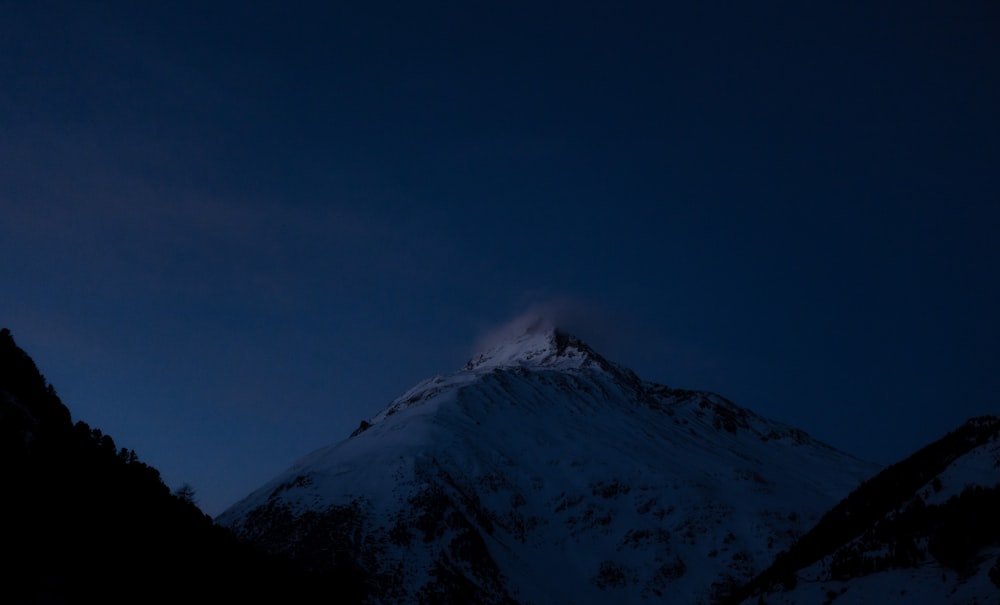 a snow covered mountain at night with the moon in the sky