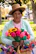 A smiling woman wearing a bright handmade crochet summer hat outdoors.