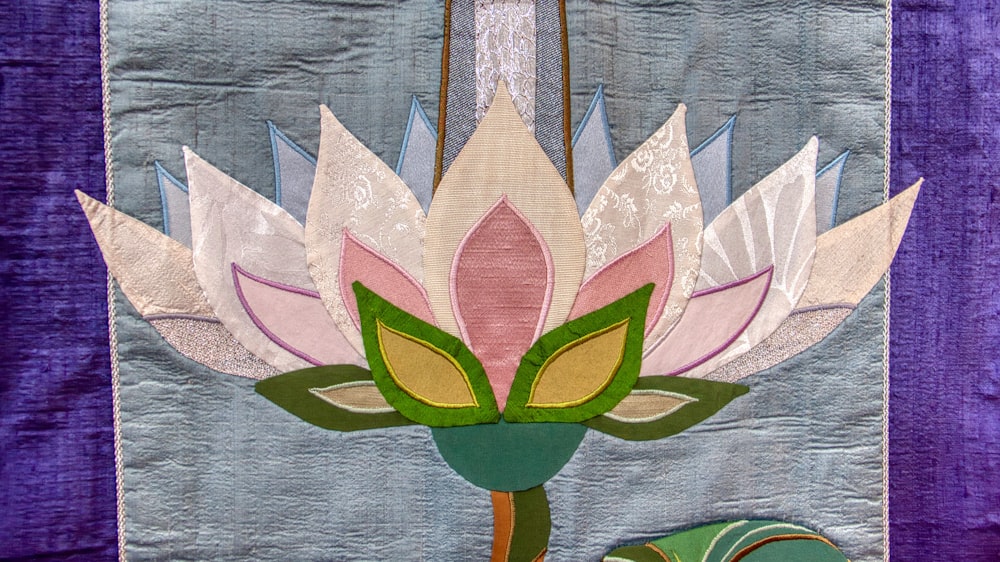 a quilted picture of a pink flower with green leaves