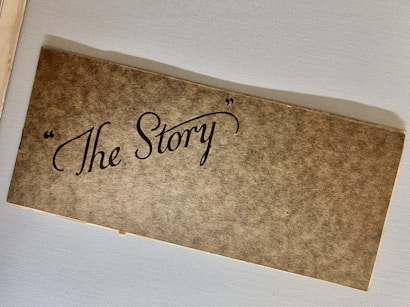 A brown, textured cardboard cover with elegant, cursive black lettering that reads 'The Story' enclosed in quotation marks. The object appears to be placed on a light gray surface.