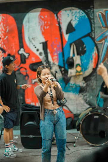 A warm photo of Liliana Baglietto speaking into a microphone at La Onda radio station, surrounded by community artwork.