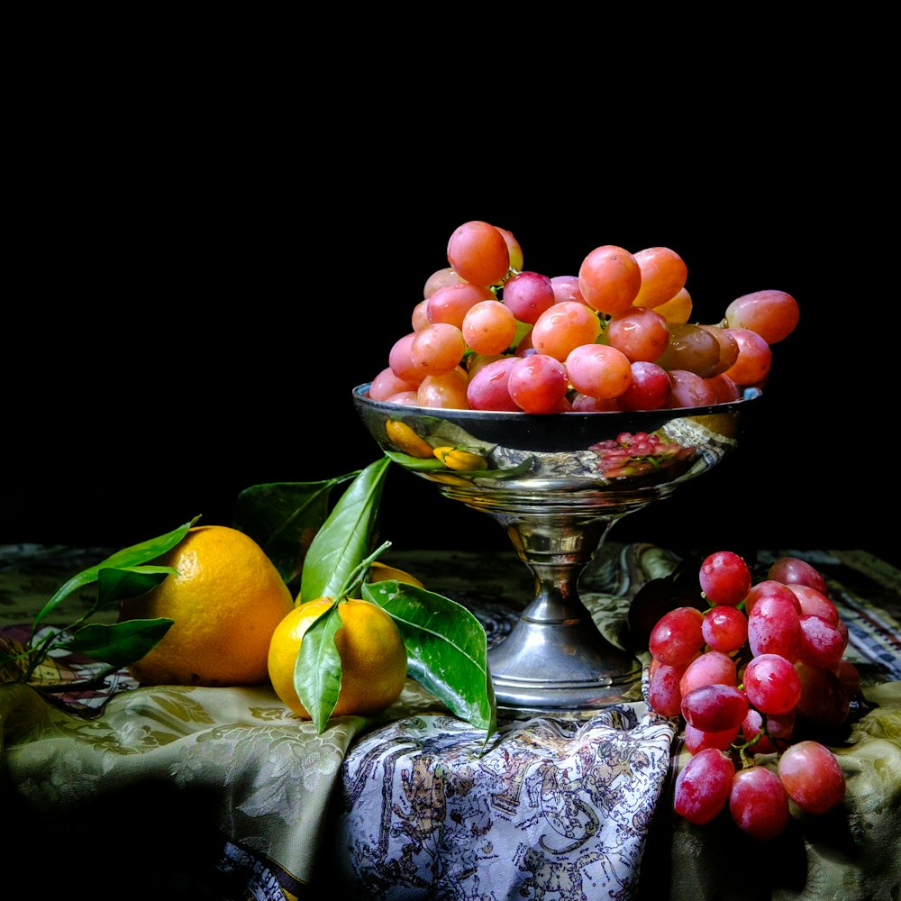 a bowl of grapes and oranges on a table