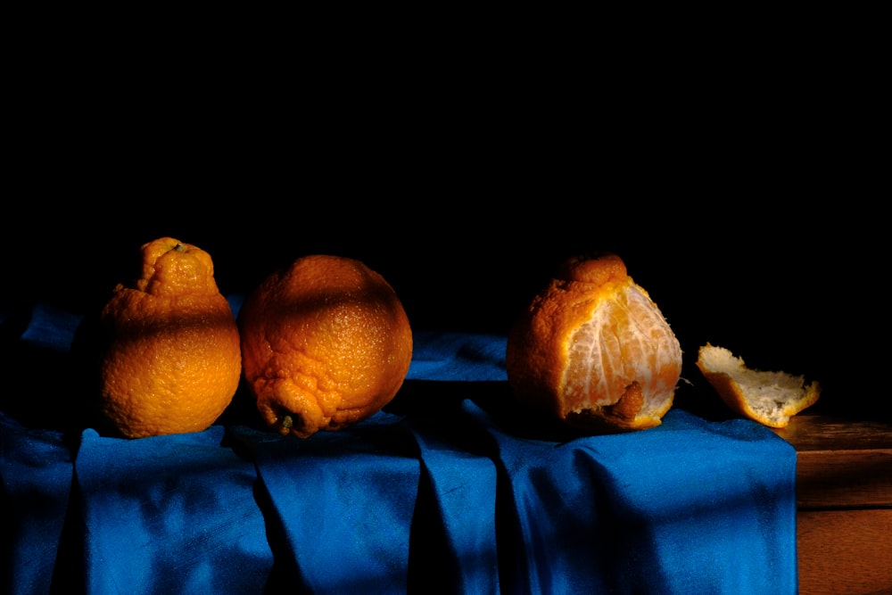 three oranges are sitting on a blue cloth