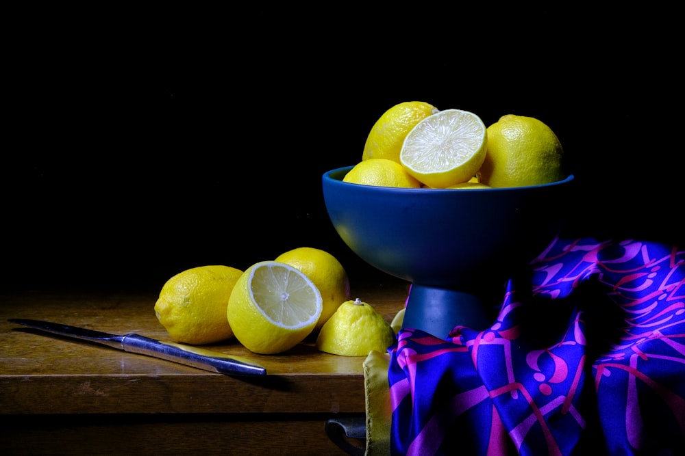 a blue bowl filled with lemons on top of a wooden table