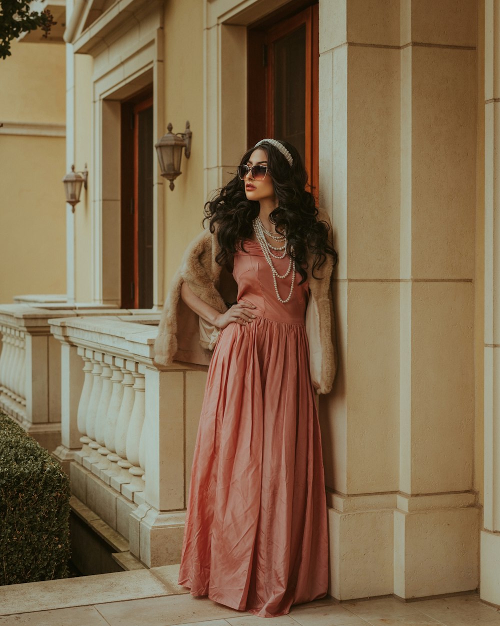 a woman in a long dress leaning against a wall